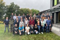 Frauen und Männer stehen neben einem Gebäude in drei Reihen auf einer Wiese