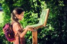 Mädchen in Wanderkleidung und Rucksack öffnet eine Klapptafel
