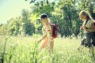 Zwei Mädchen in Wanderkleidung und Rucksäcken wandern durch hohe Wiese